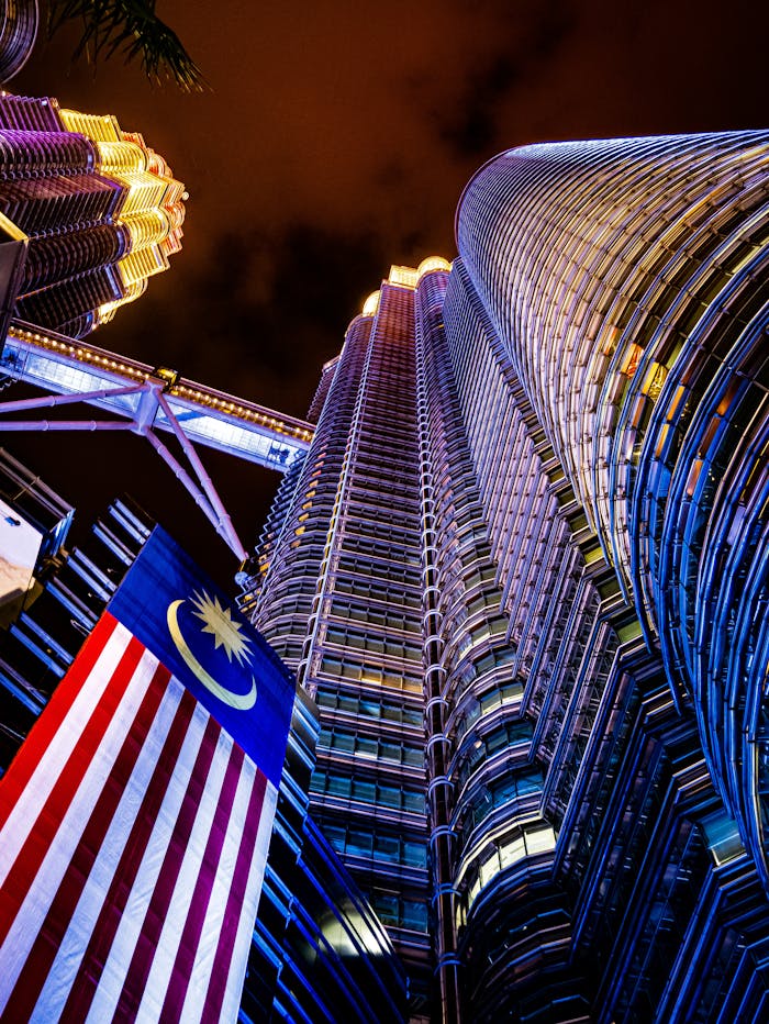 team-03 Dramatic view of Petronas Twin Towers illuminated at night with the Malaysian flag.
